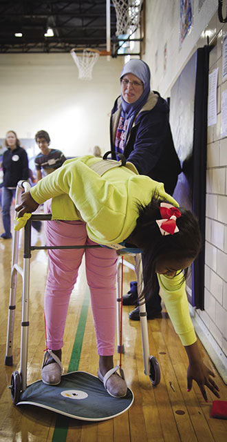 Sixth-grader Tiara Anderson struggles to reach a bean bag after being outfitted with a walker and leg restraints, one of several SAGE workshop exercises to teach empathy for students with disabilities. Photo by Kim Leeson