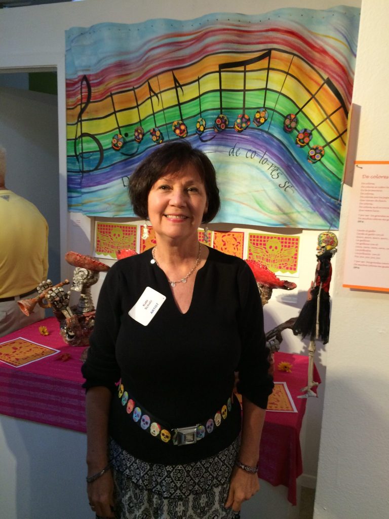 Artist Kate Schatz poses in front of her piece "De Colores." The mixed media piece displays the actual music notes from the popular children's song "De Colores." Schatz teaches at  Northridge Elementary in Richardson ISD and her sister co-owns Gecko Hardware. This is her 13th year displaying artwork in the show.