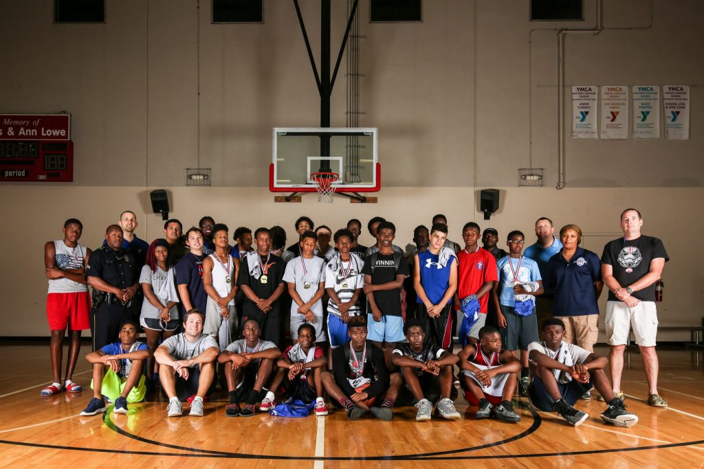 Players and volunteers have a group photo taken at the Lake Highland Family YMCA. The group is composed of the handful of volunteers, including Dallas Police Department officers from the PALS division, who are connecting with at-risk youth in a summer pilot basketball program. (Photo by Rasy Ran)