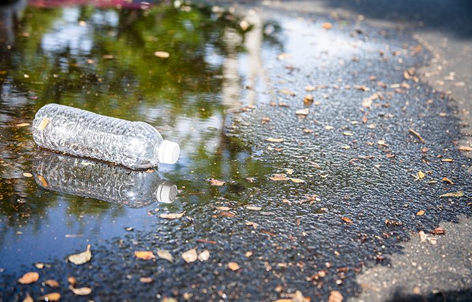 Pollution themes. An empty, plastic water bottle is discarded in rain puddle on an empty city street. No people. Recycling, pollution, environmental conservation themes.