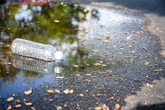 Pollution themes. An empty, plastic water bottle is discarded in rain puddle on an empty city street. No people. Recycling, pollution, environmental conservation themes.