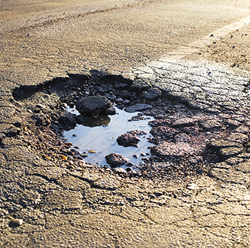A road damaged by rain and snow, that is in need of maintenance. Broken asphalt pavement resulting in a pothole, dangerous to vehicles.