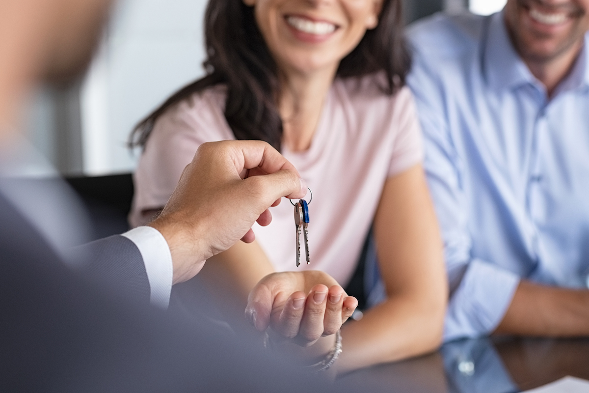 Close up of man hand giving house keys to woman. Smiling mature woman receiving new house keys from real estate agent. Man delivering keys to client for new home. Real estate agent giving keys to apartment owner.