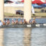 Dallas United Crew varsity boys rowing. There are eight of them, and the blades of their oars are in the air as they prepare to take a stroke.