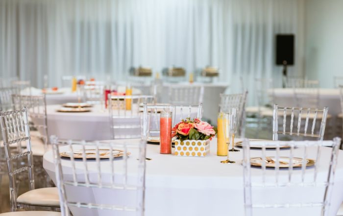 Several tables at the Blank Space Venue set with plates and silverware. Each has a centerpiece of flowers and candles.