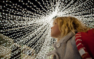 A girl looks upwards at white Christmas lights