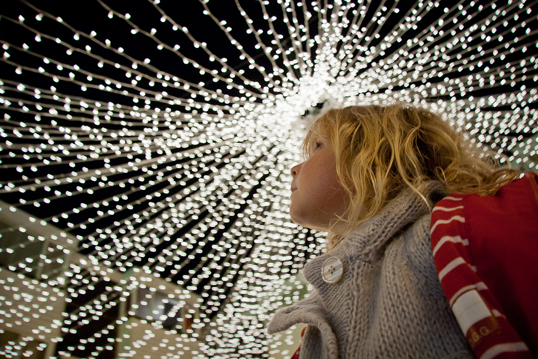 A girl looks upwards at white Christmas lights